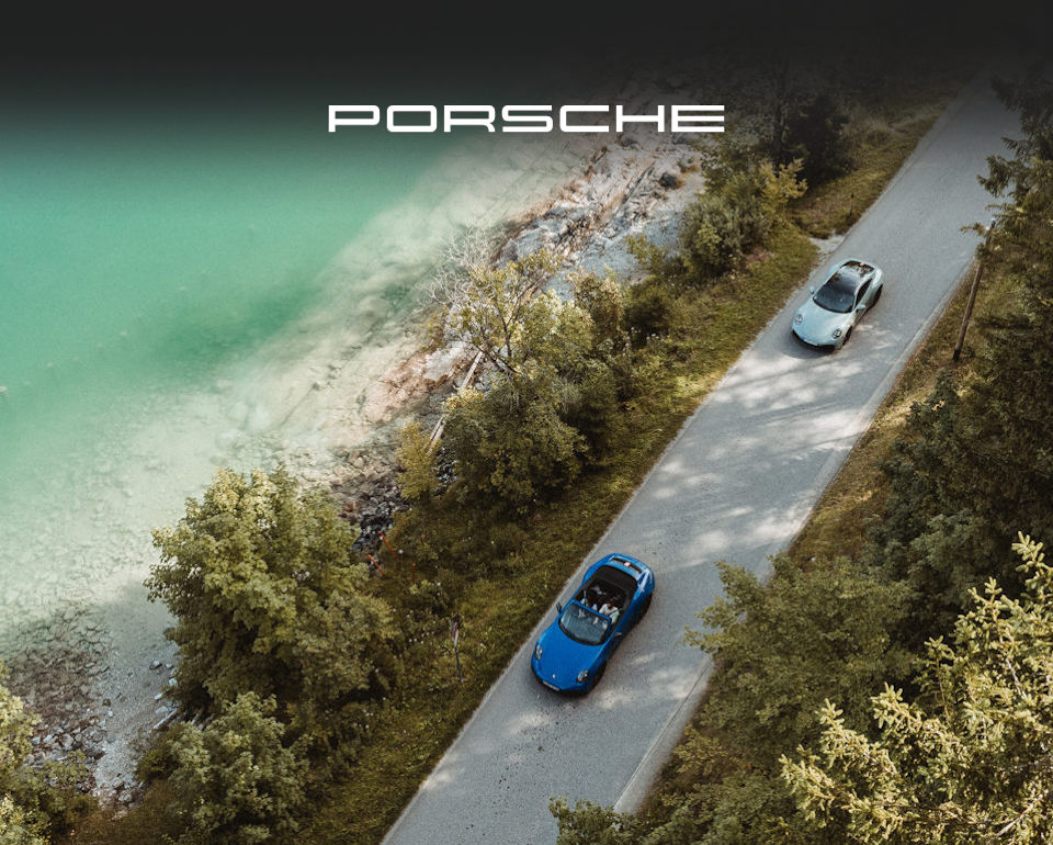Two Porsche cars on a winding lakeside road